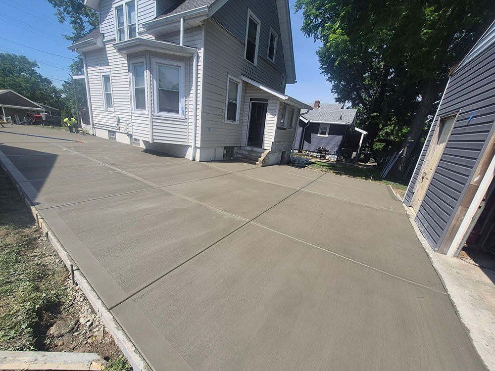 Fresh concrete driveway beside a white house and garage on a sunny day