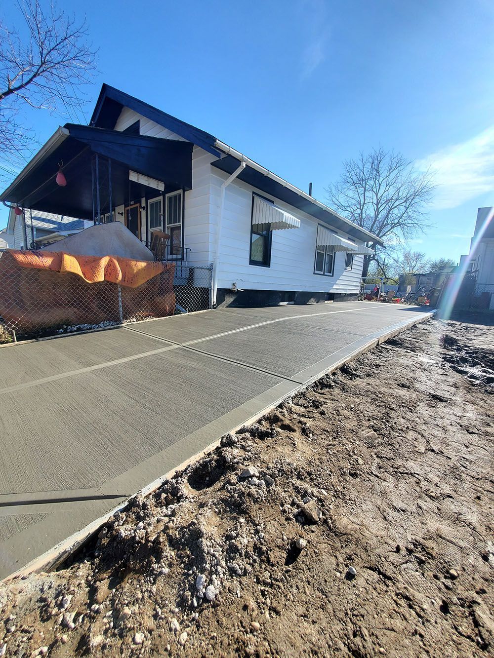 Damaged white house beside a cracked sidewalk and dirt mound under a blue sky
