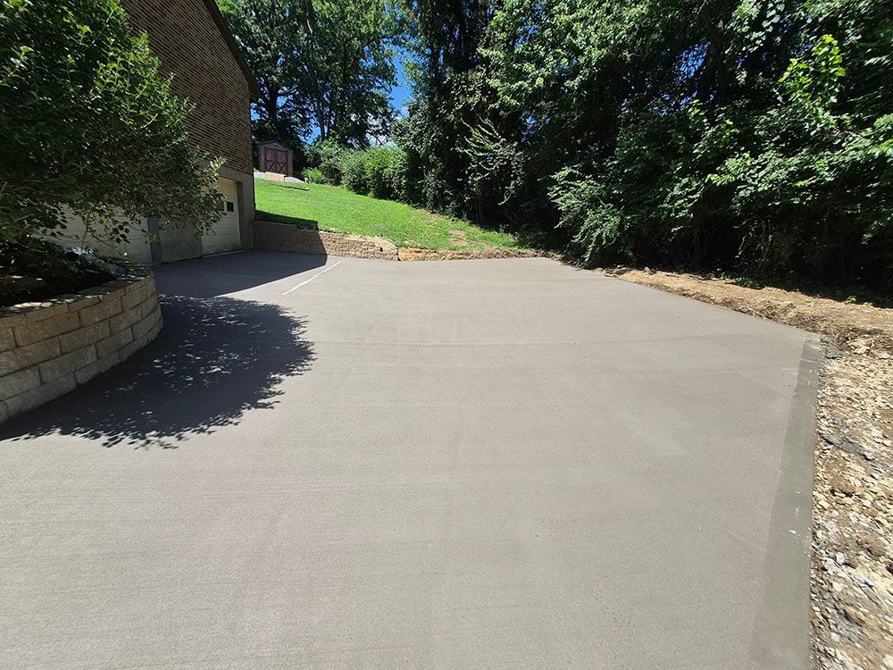 New concrete driveway curving uphill beside a stone wall and trees on a sunny day