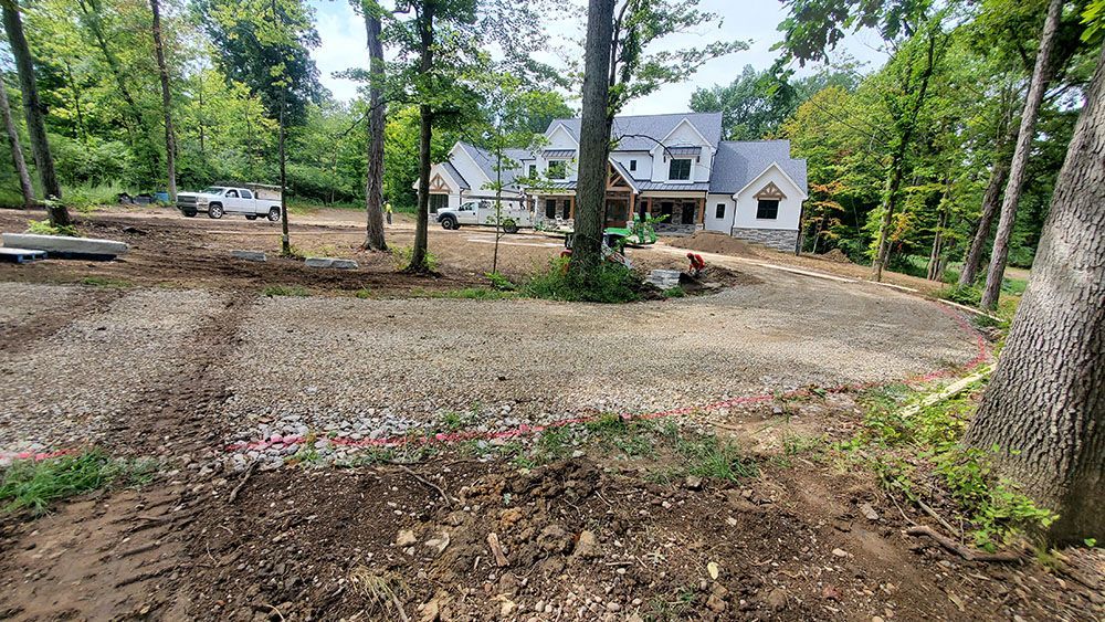 Large gravel driveway leading to a white house surrounded by trees in a wooded suburban setting