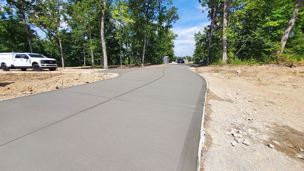 Paved road under construction in a wooded area, with a white truck parked on the left.