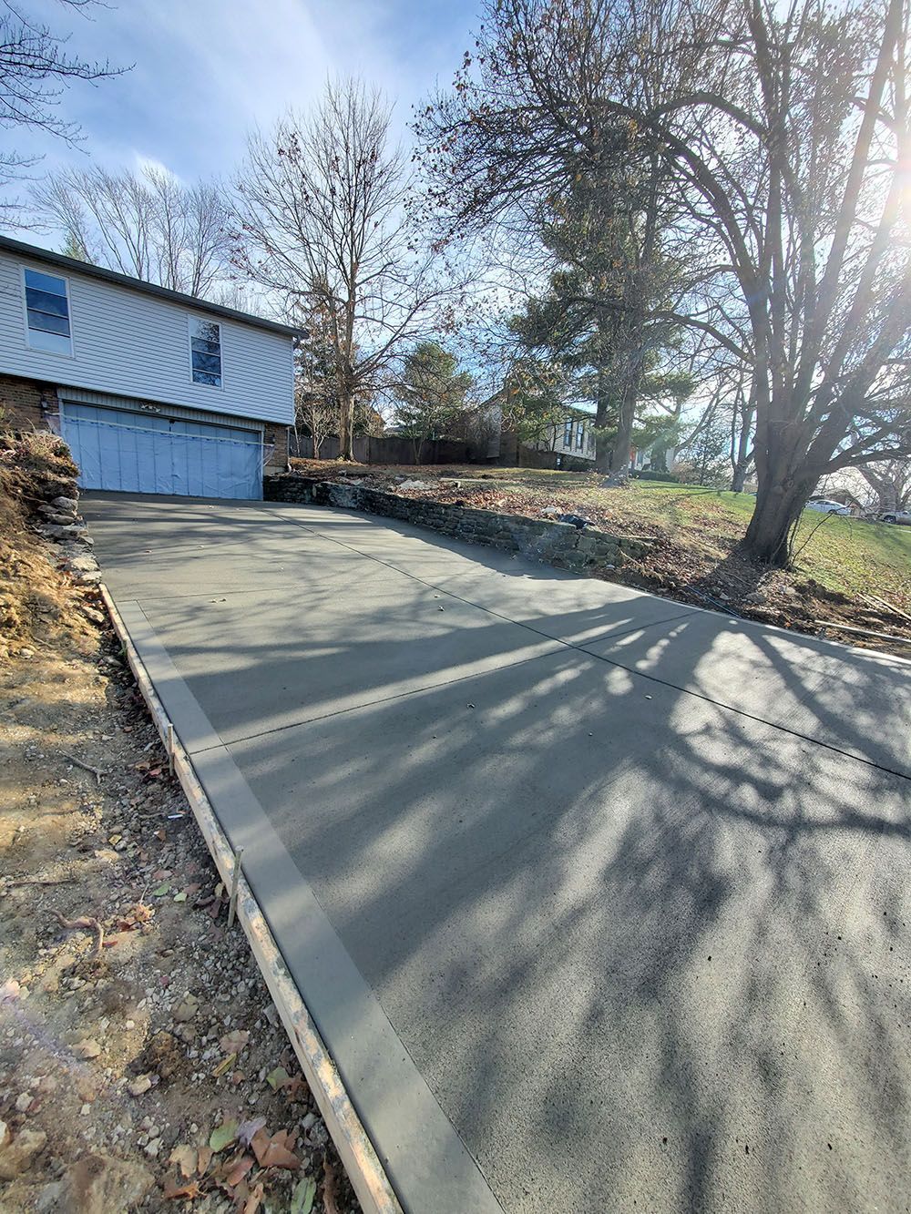 New concrete driveway beside a blue garage on a sunny residential property