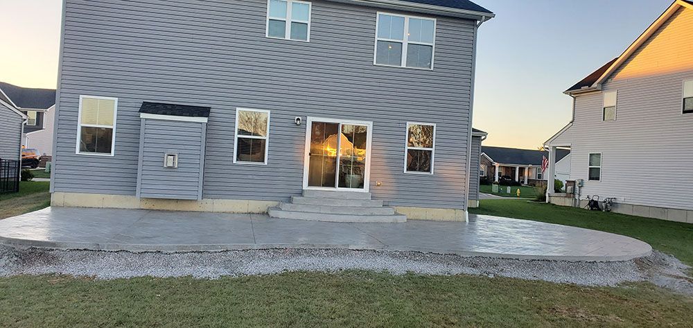 Backyard view of a gray two-story house with sliding glass doors and a concrete patio at dusk