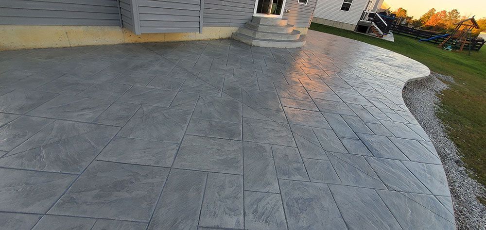 Stamped concrete patio beside a house at sunset, with steps, siding, and a grassy yard