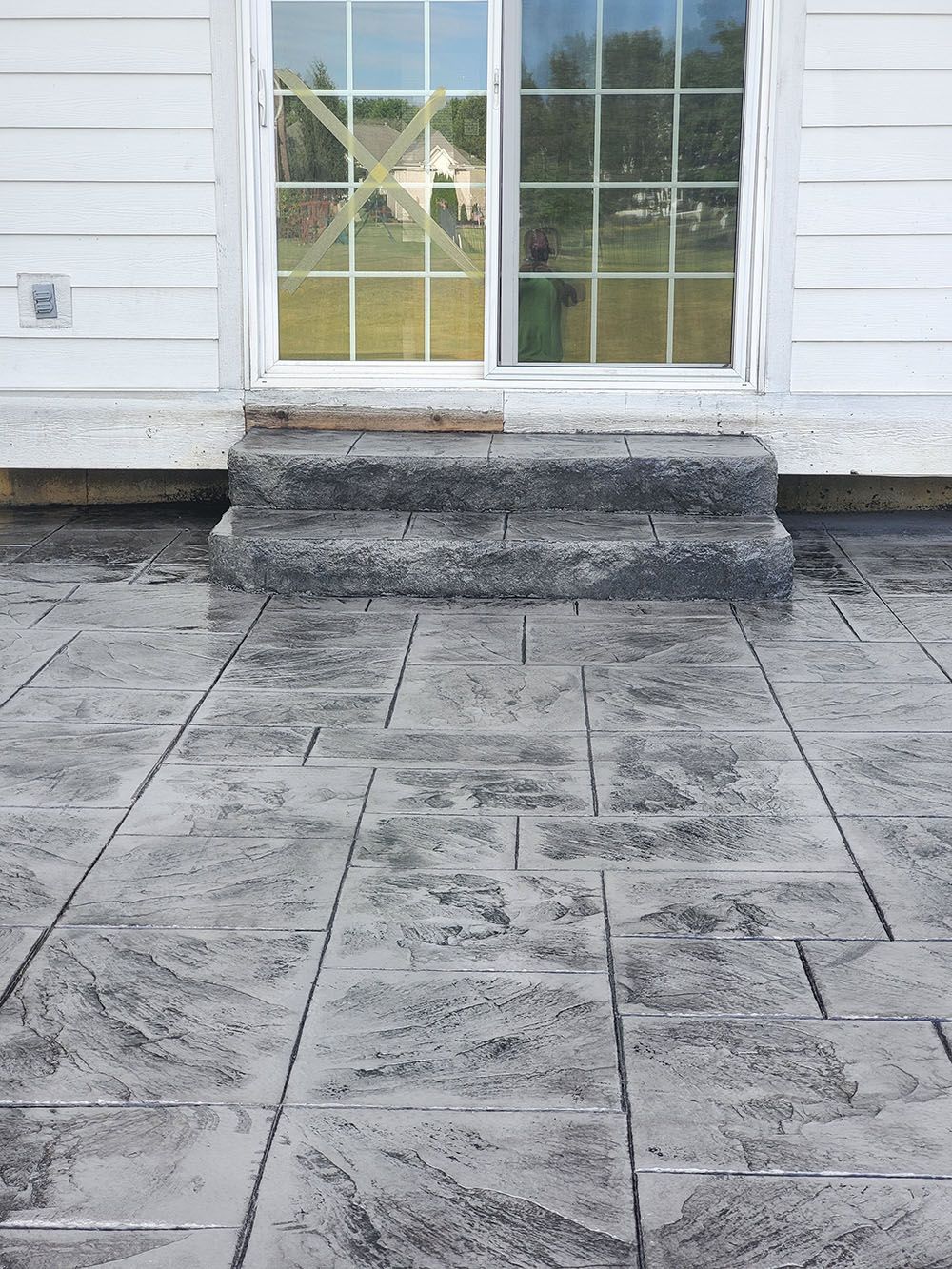 White house exterior with a single window and three stone steps leading to a patterned patio.