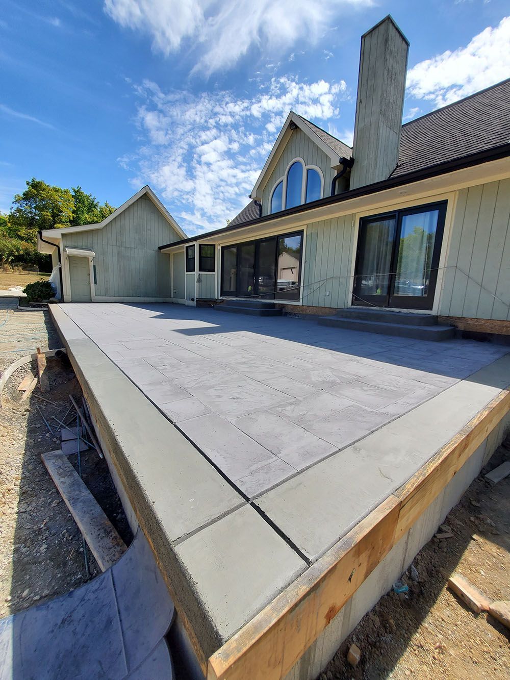 Concrete patio beside a house with a chimney, sliding doors, and a detached garage under a blue sky