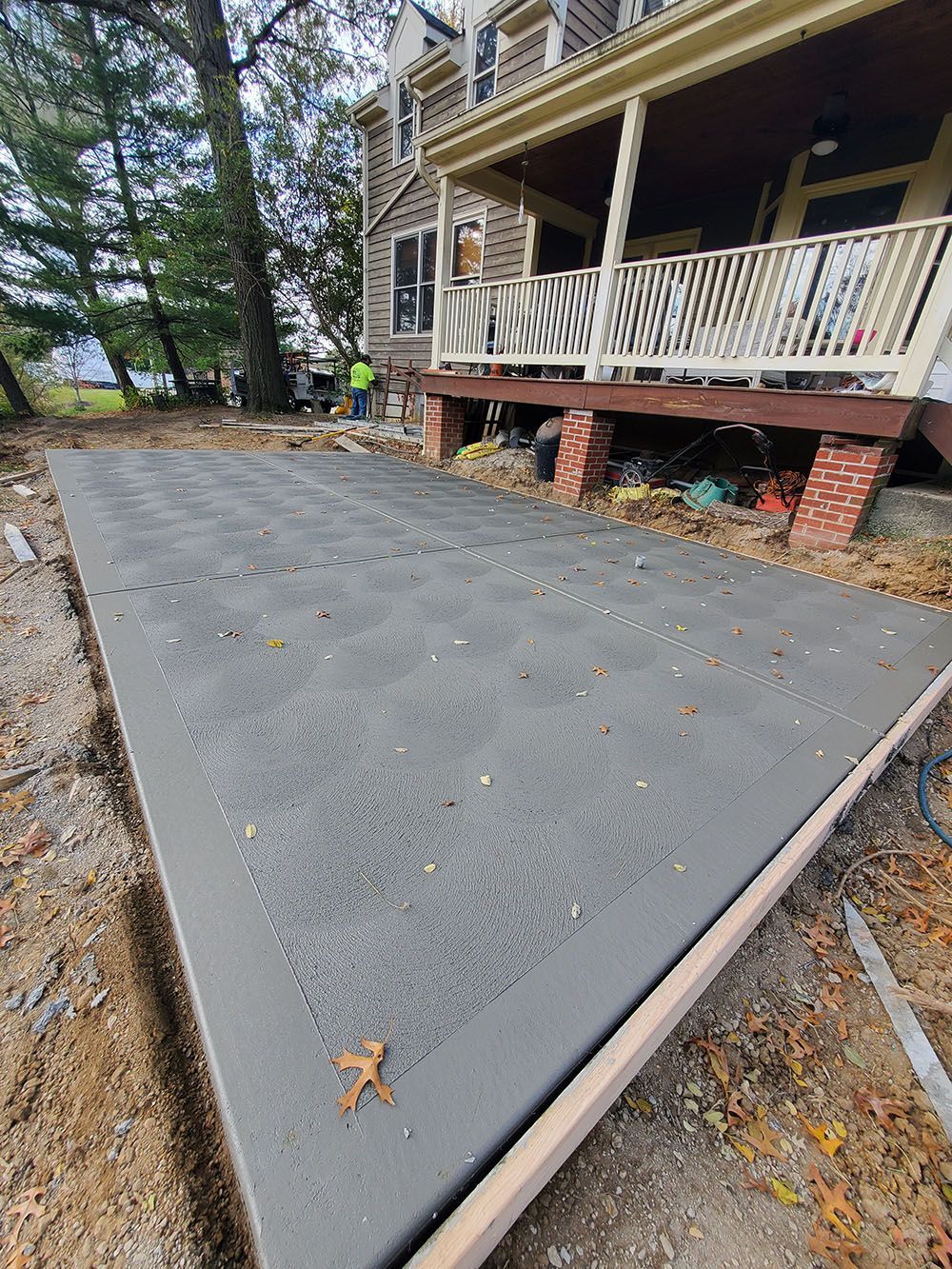 Freshly poured concrete patio beside a raised wooden porch and stone foundation