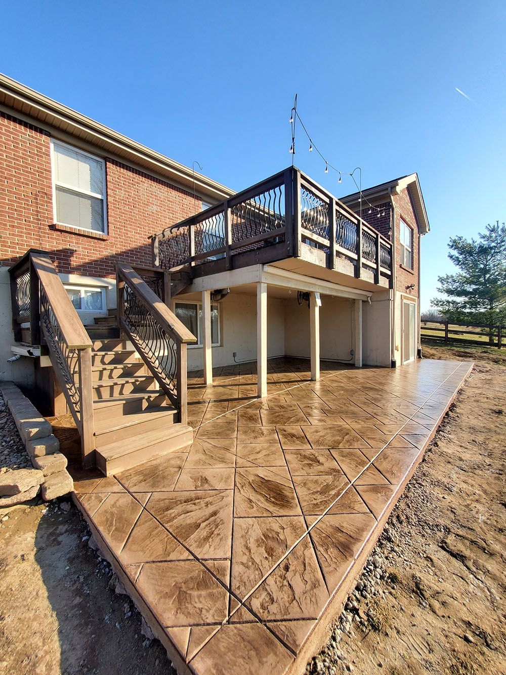 Brick house deck with stairs, white support posts, and a wet concrete patio under construction
