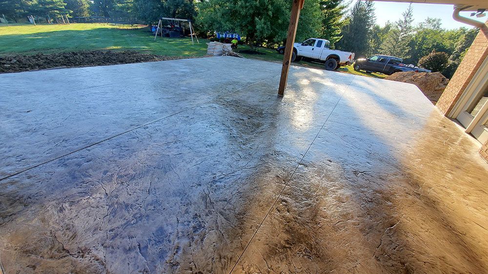 Sunlit wet concrete driveway beside a house, with a white pickup truck and trees in the background.
