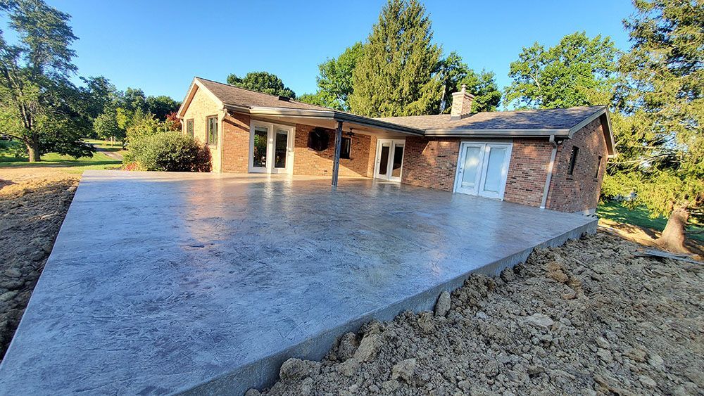Fresh concrete driveway slab beside a brick house in a wooded yard