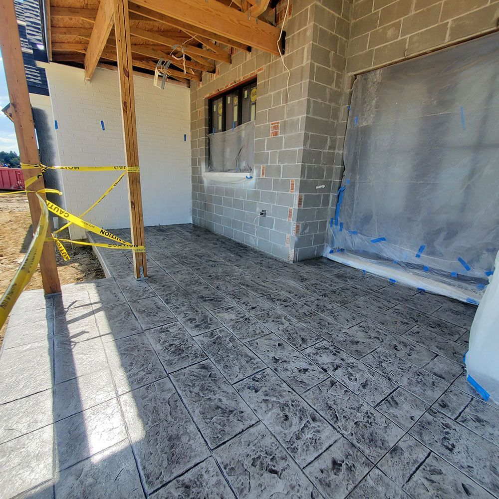Covered outdoor patio with stamped concrete floor, cinderblock wall, and partially taped-over window and doorway.