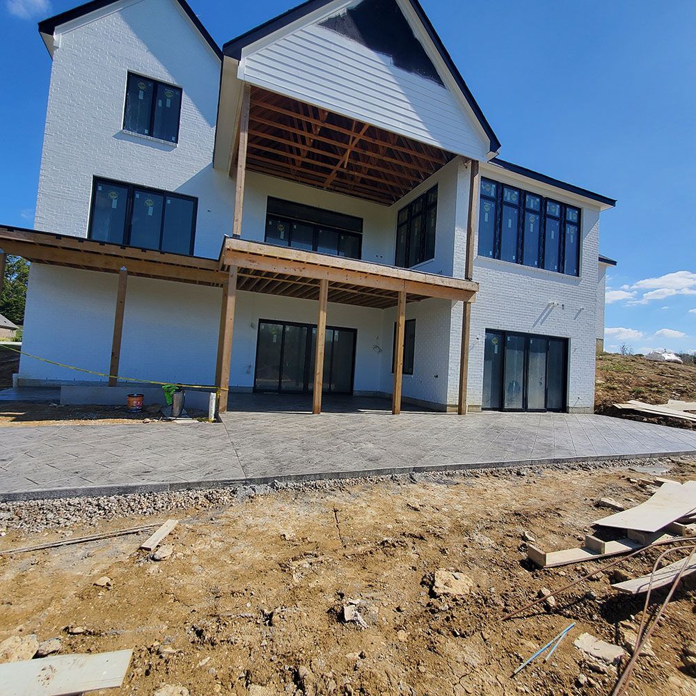 Modern two-story house under construction with white walls, dark windows, and a gravel and dirt foreground.