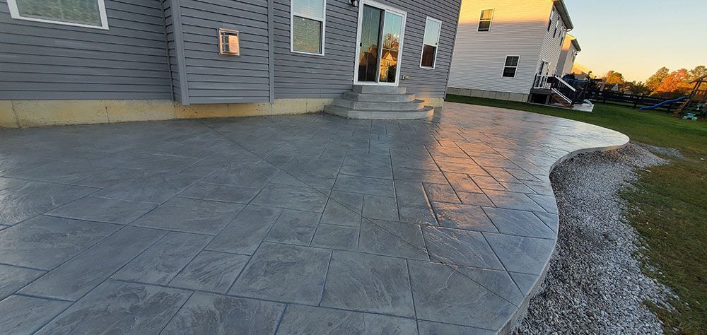 Stamped concrete patio beside a house at sunset, with a curved edge and wet-looking surface.