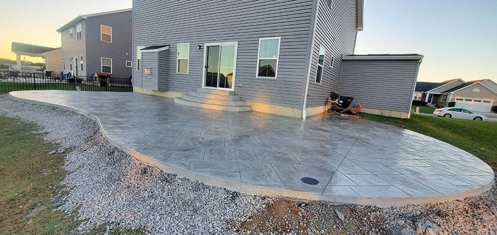 Concrete patio beside a gray house with windows, viewed at sunset
