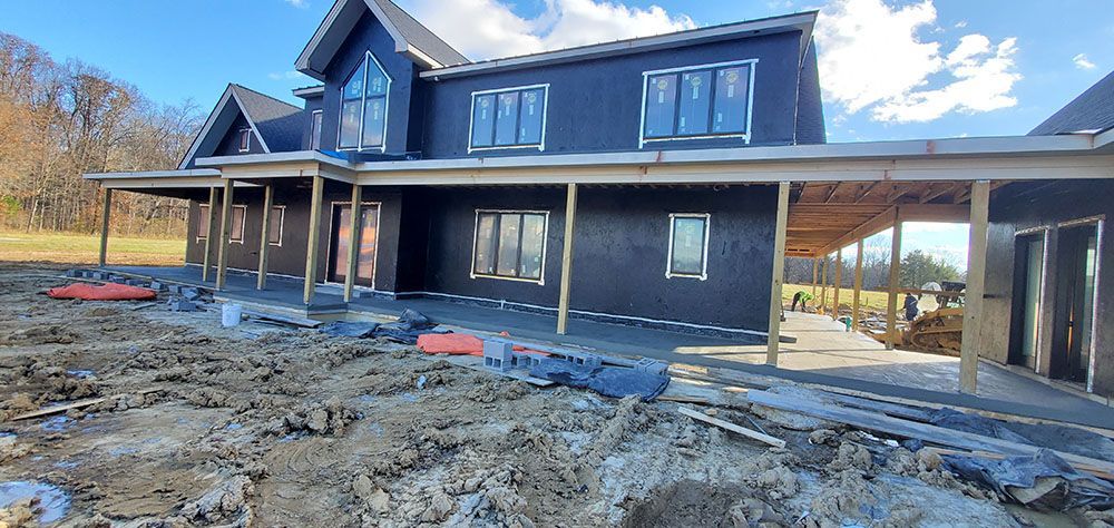 Partially built dark blue house with unfinished yard and covered porch under a bright sky