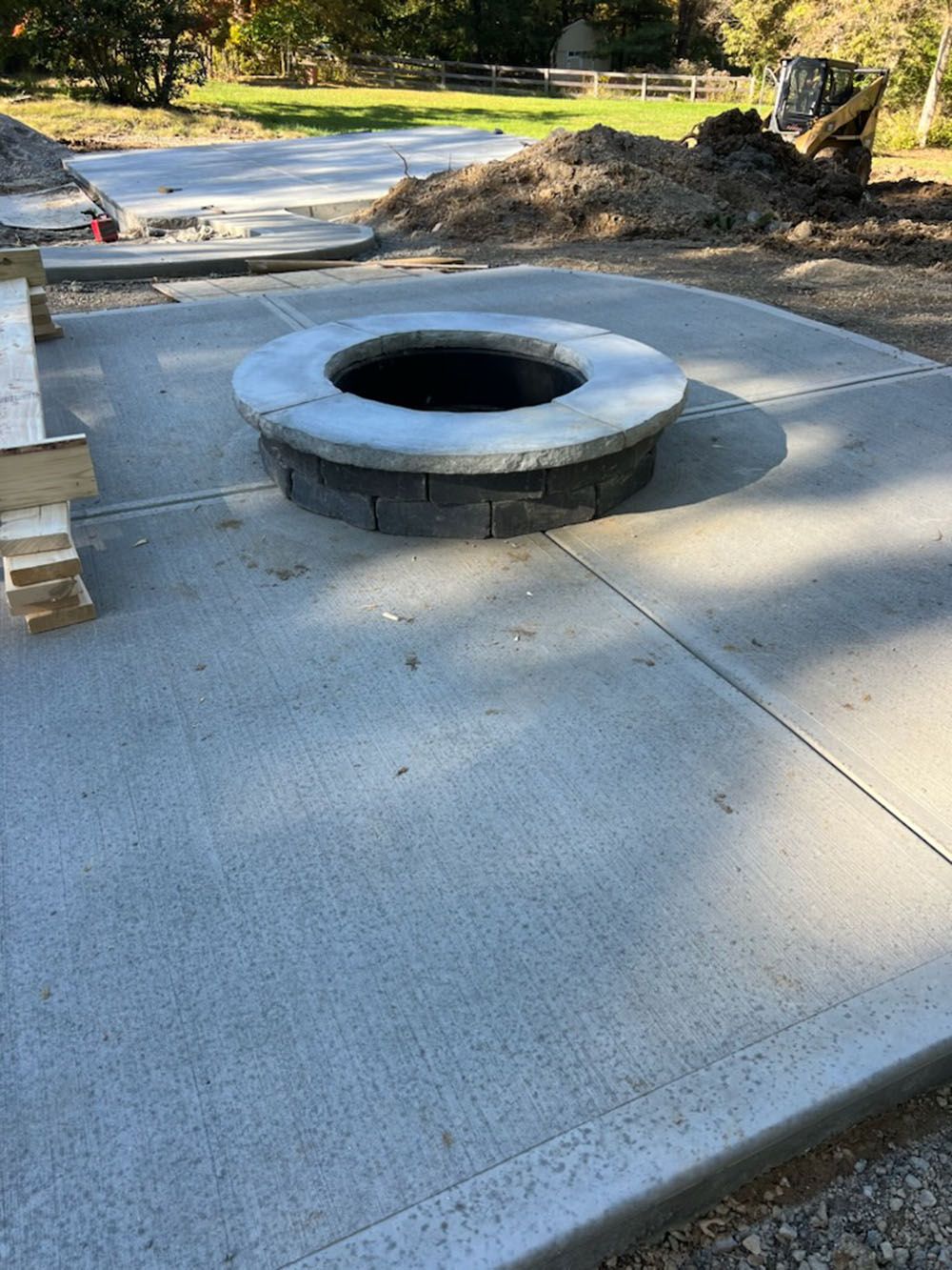 Concrete fire pit ring on a newly poured patio in a yard.