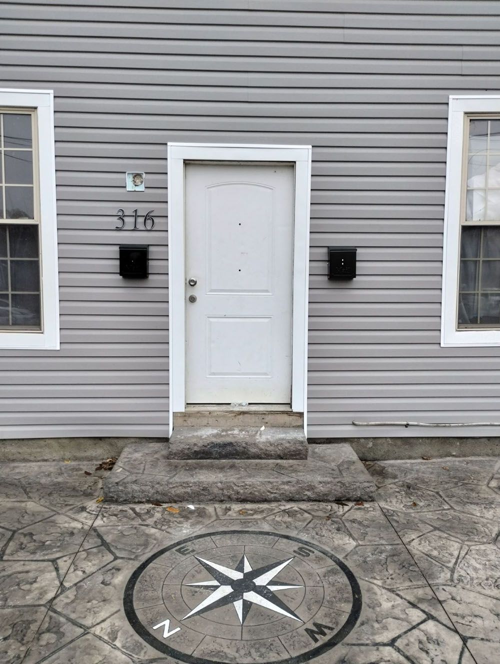 Front entrance of a gray house with a white door, windows, and a compass rose in the stone walkway.