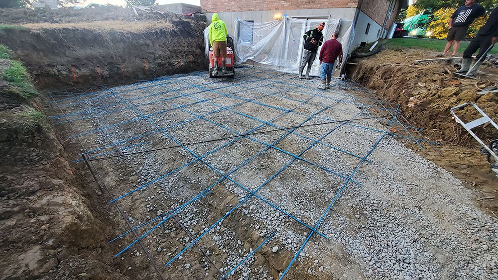 Workers pouring concrete and laying rebar in a foundation trench at a construction site