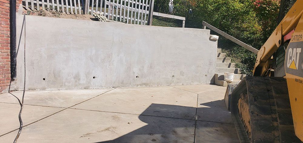 Outdoor construction site with a white retaining wall, concrete ground, and a CAT machine at right