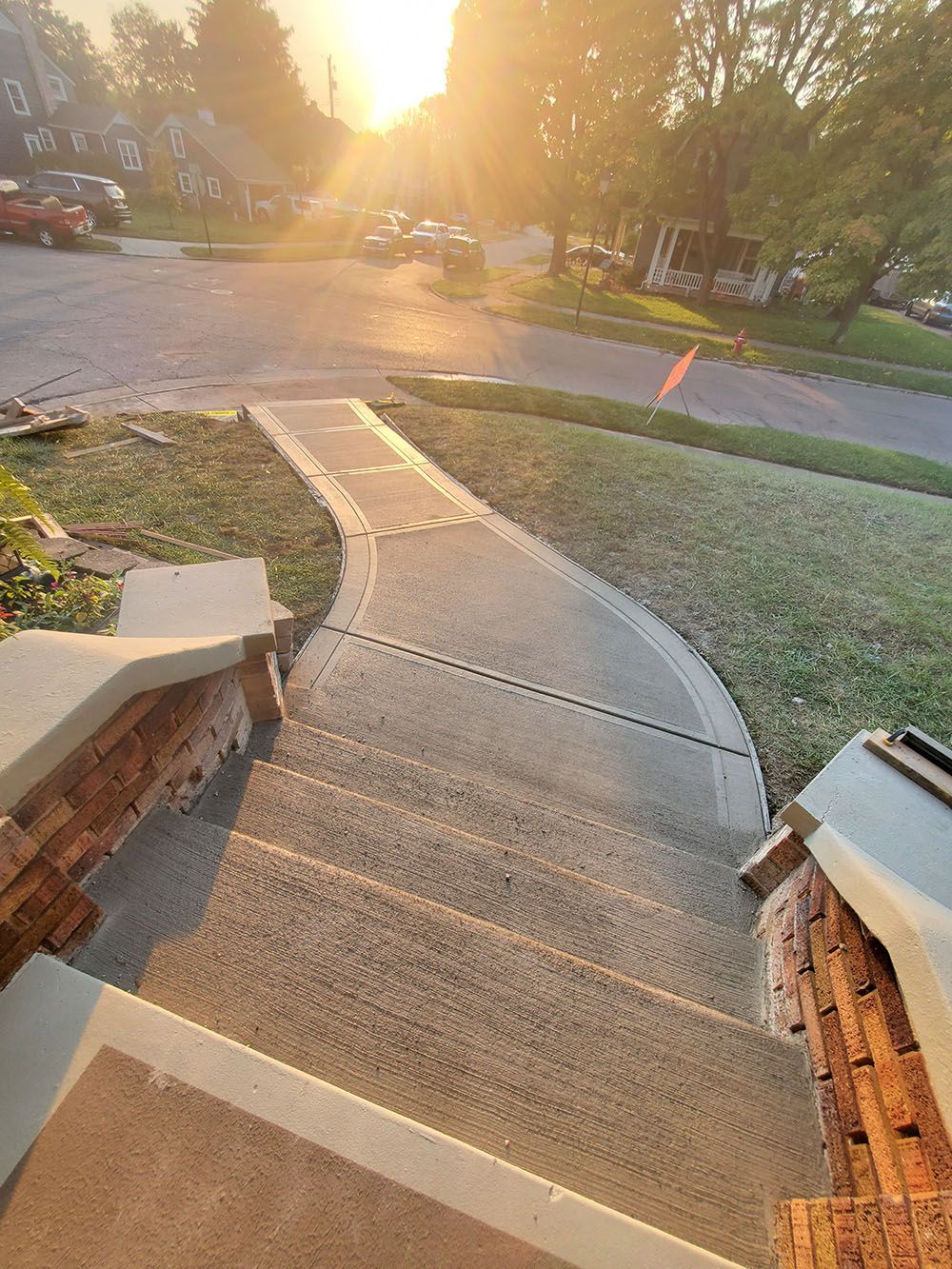 Curved concrete walkway descending to a street at sunset, bordered by brick and grass.