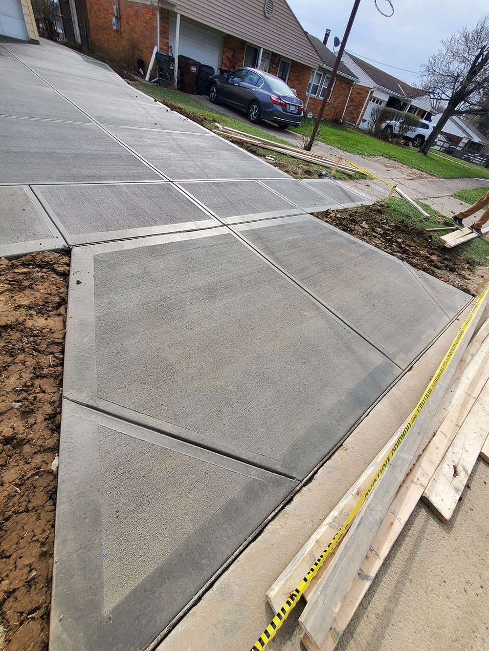 Sidewalk corner with fresh concrete, a small curb ramp, and yellow caution tape along the edge.