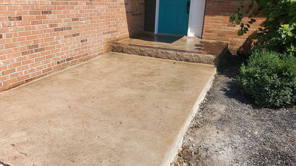 Concrete patio beside a brick house, with a teal door and small stone step.