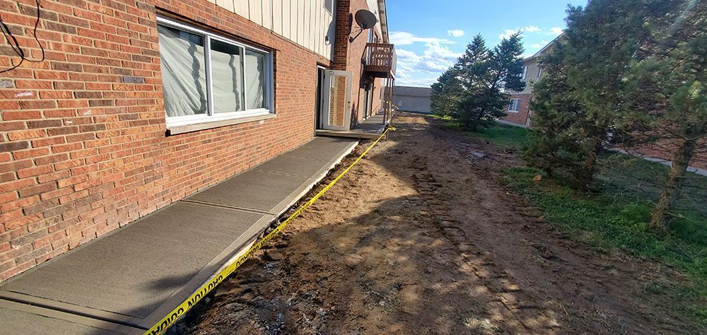 Brick building walkway beside muddy dirt strip and trees under a bright sky
