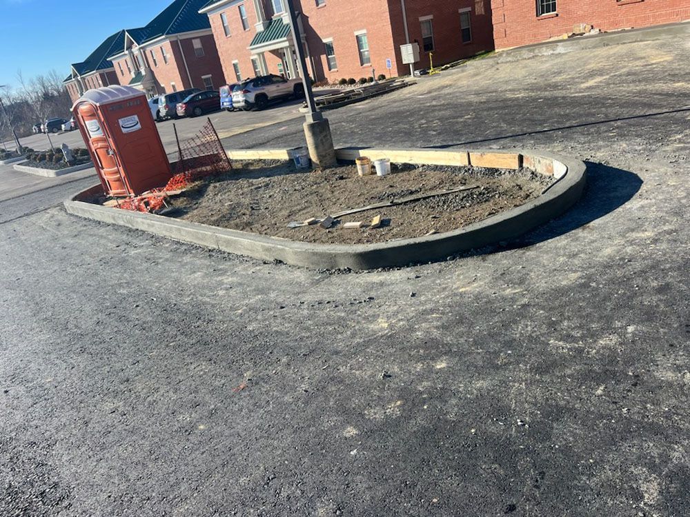 Damaged curb around a dirt island near brick houses and a red utility box on a paved street