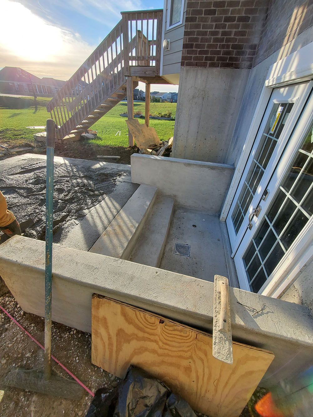 Concrete steps and foundation beside a brick house under construction, with a wooden railing and stairs in the background