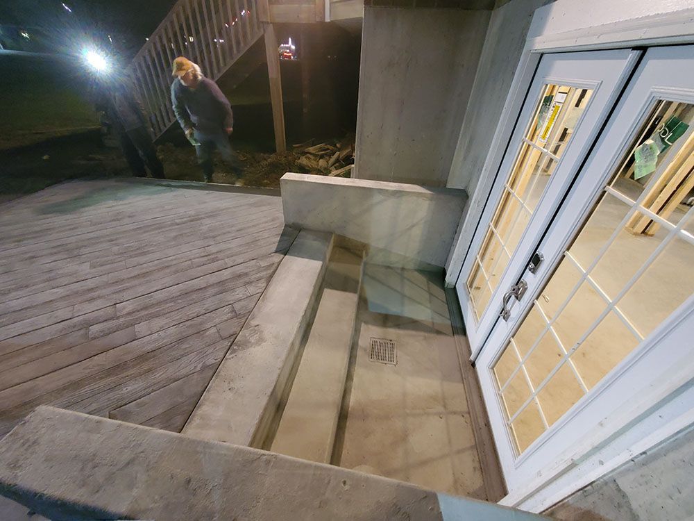 Outdoor wooden deck beside a house, with steps, railing, and a person near the stairs at night.