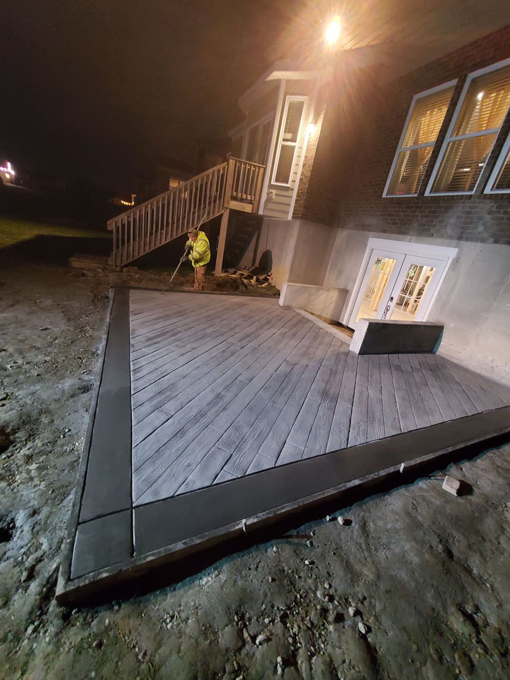 House exterior with a newly built wooden deck and stairs at night, with a worker near the steps
