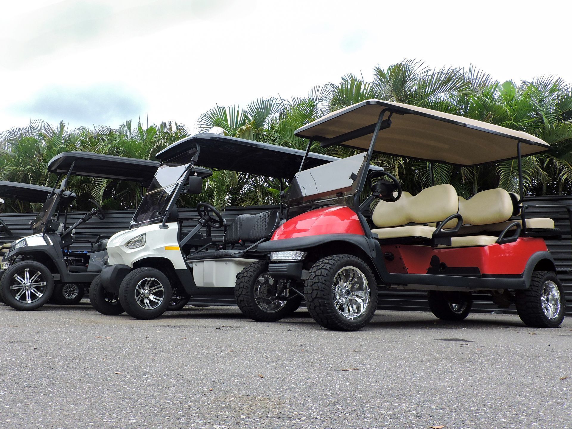 Three parked golf carts in a lot, including red, white, and black carts with roofs and beige seats