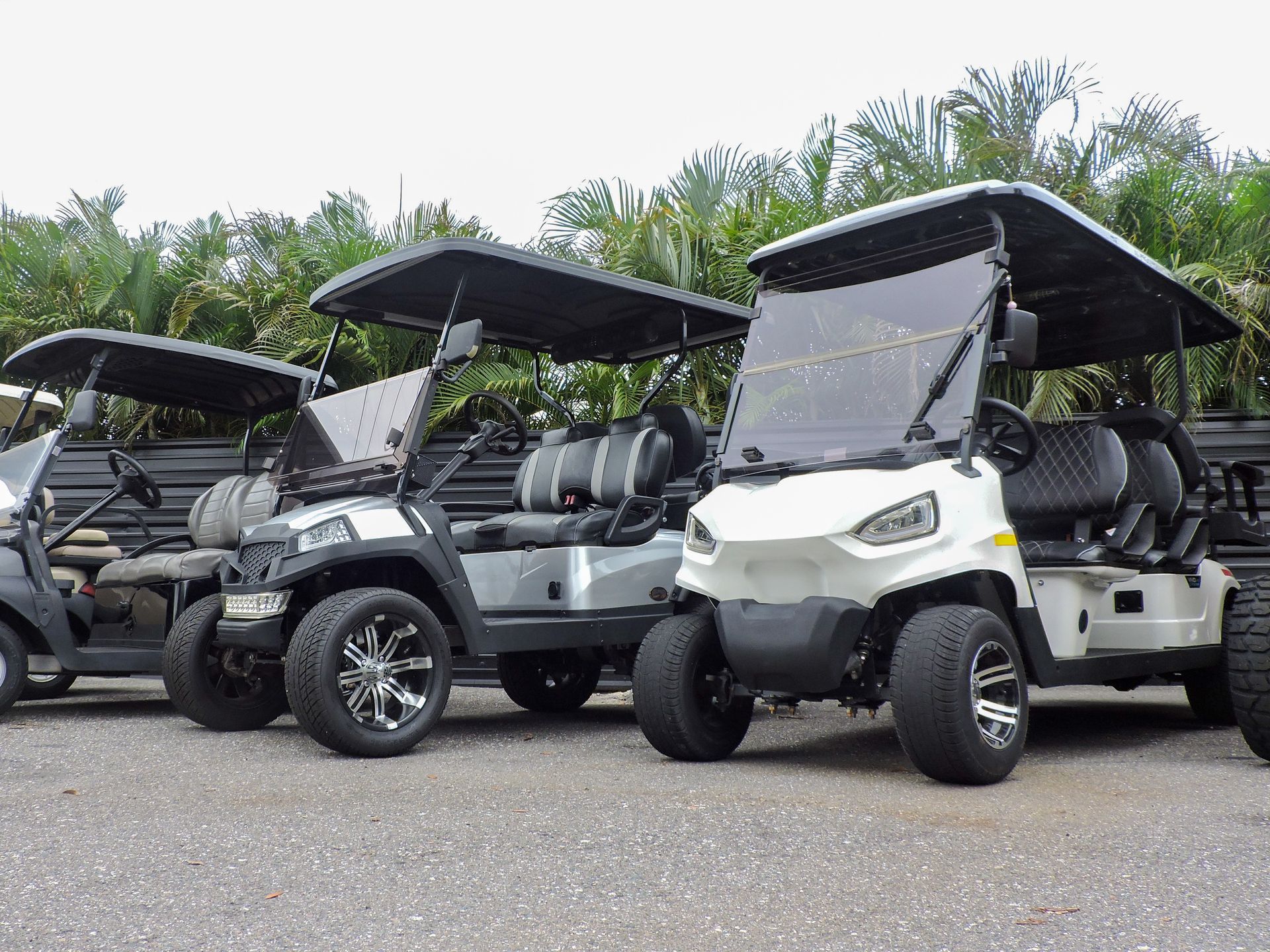 Three parked white and black golf carts with canopies on a paved lot, trees in the background
