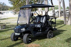 Black golf cart on grass with black and gray seating and a windshield.