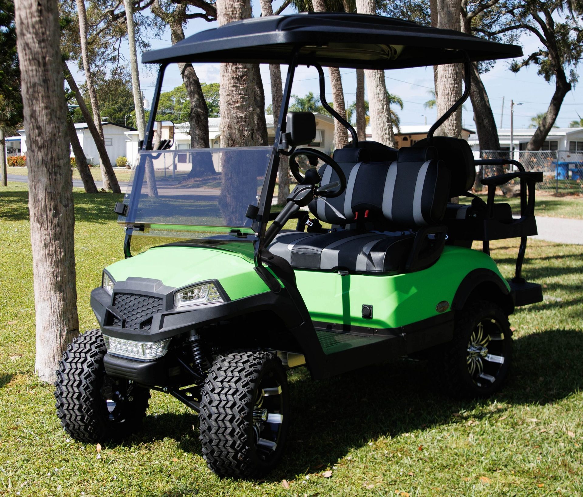 Green and black golf cart with a black roof, parked on grass.