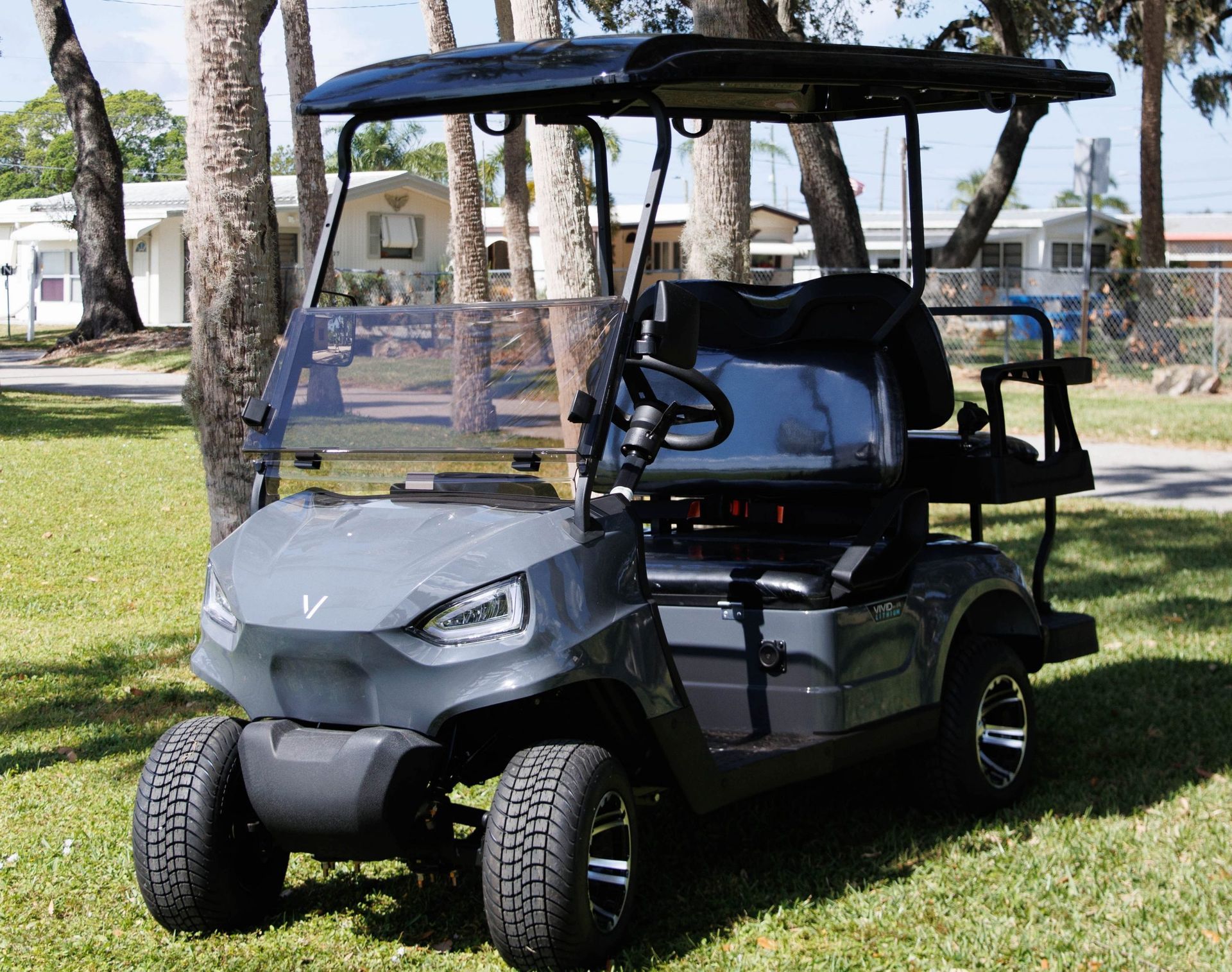 Gray golf cart with black canopy, parked outdoors on a sunny day.