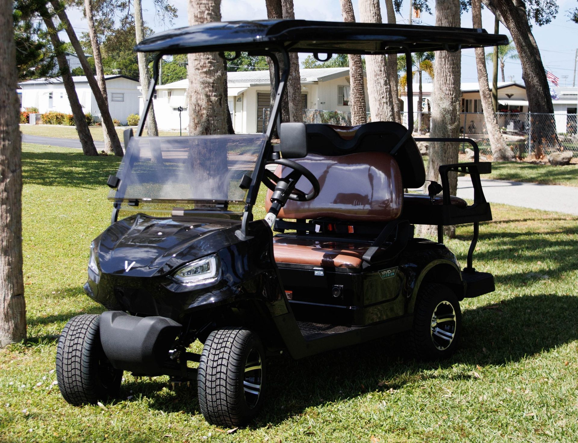 Black golf cart with brown seats parked on grass, trees in background, sunny day.