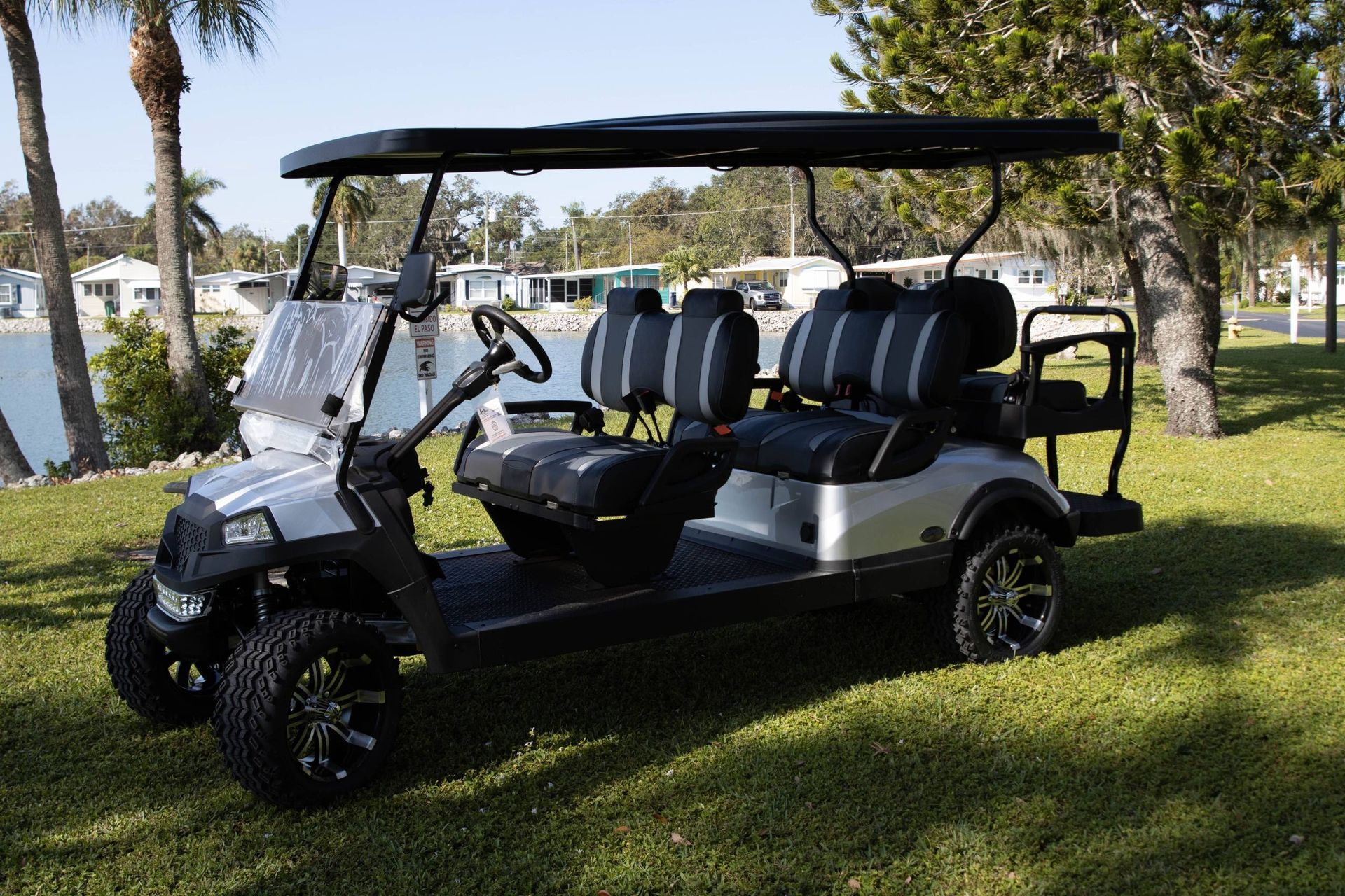 Silver golf cart with black accents, six seats, and lifted tires, parked on grass.