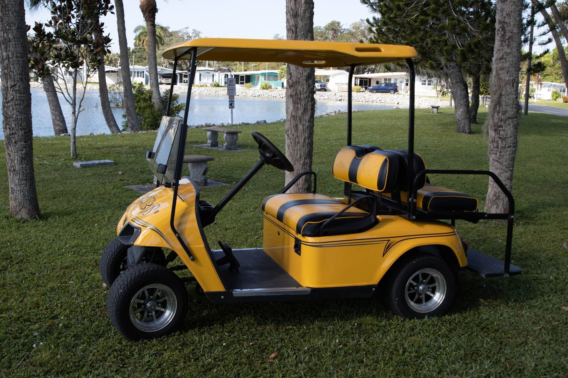 Yellow golf cart with black accents parked on grass near a lake.