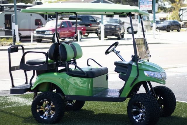 Green golf cart with lifted wheels and a canopy, parked outdoors.
