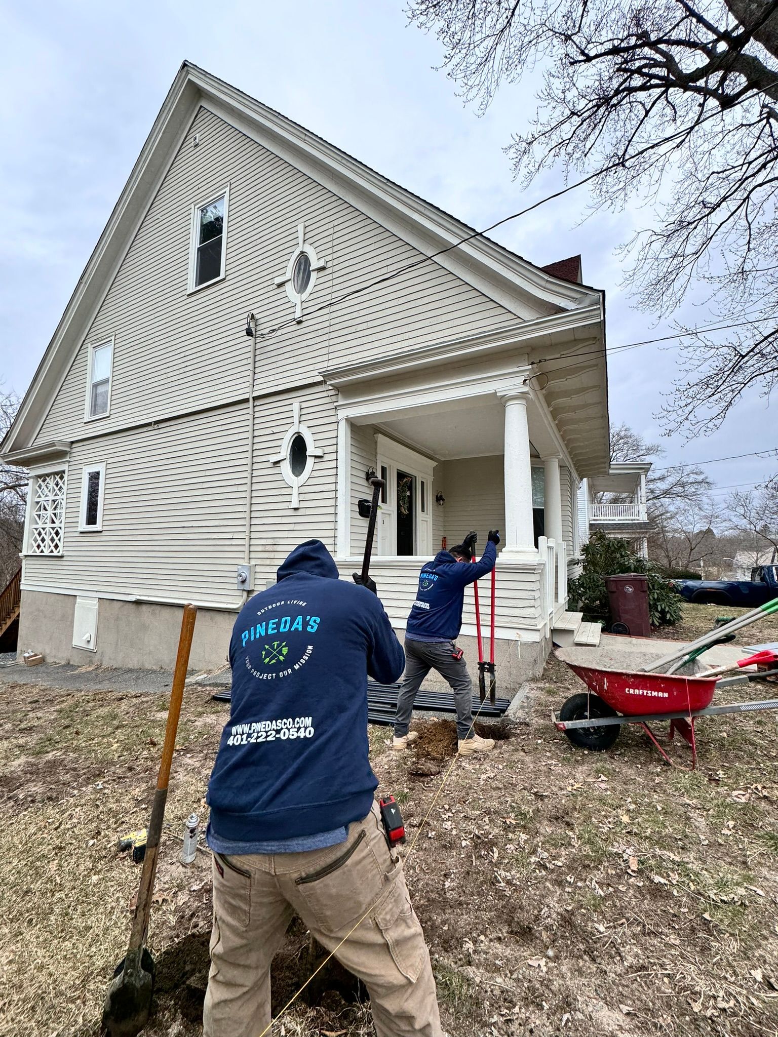 Pineda's Outdoor Living team installing a fence at a residential property. Two workers in branded hoodies digging post holes and aligning the layout for a durable and professionally installed fence. High-quality fencing services in progress.