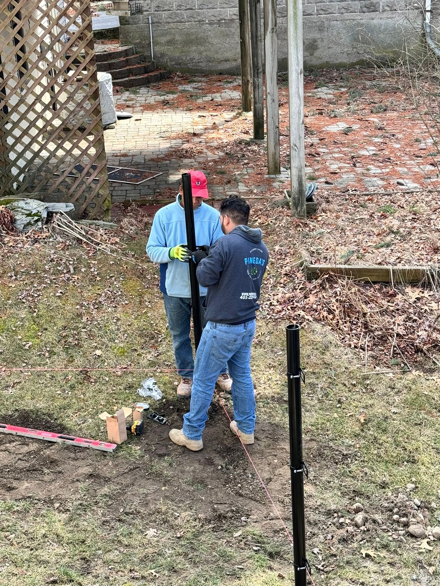 Pineda's Outdoor Living team installing a fence at a residential property. Two workers in branded hoodies digging post holes and aligning the layout for a durable and professionally installed fence. High-quality fencing services in progress.