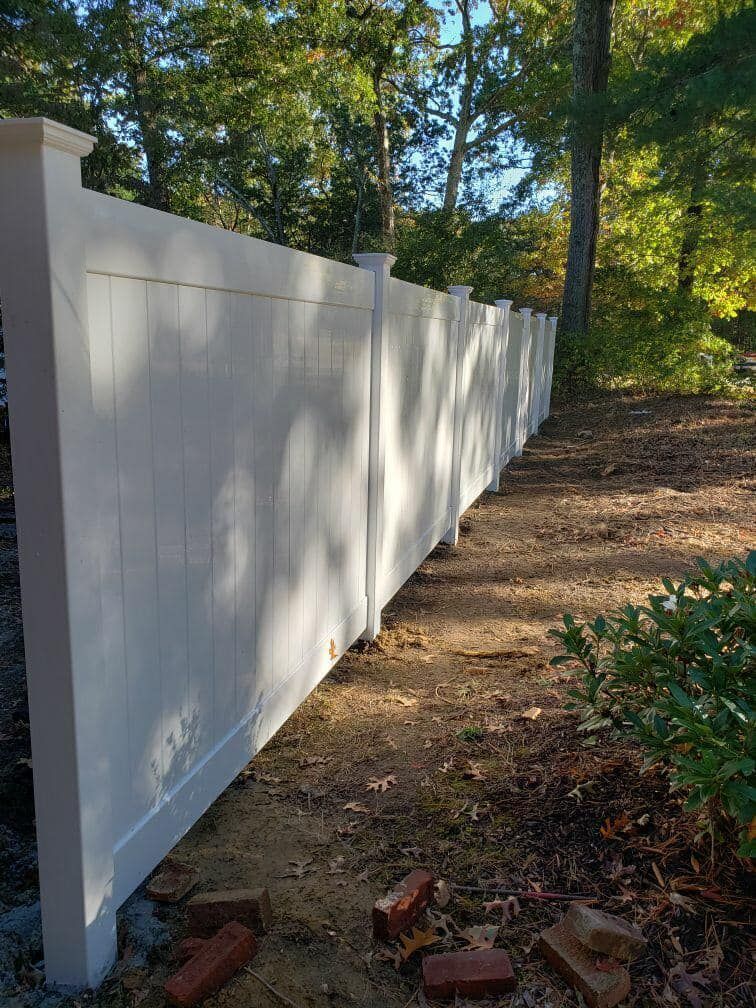 a white vinyl fence is sitting on top of a dirt hill .