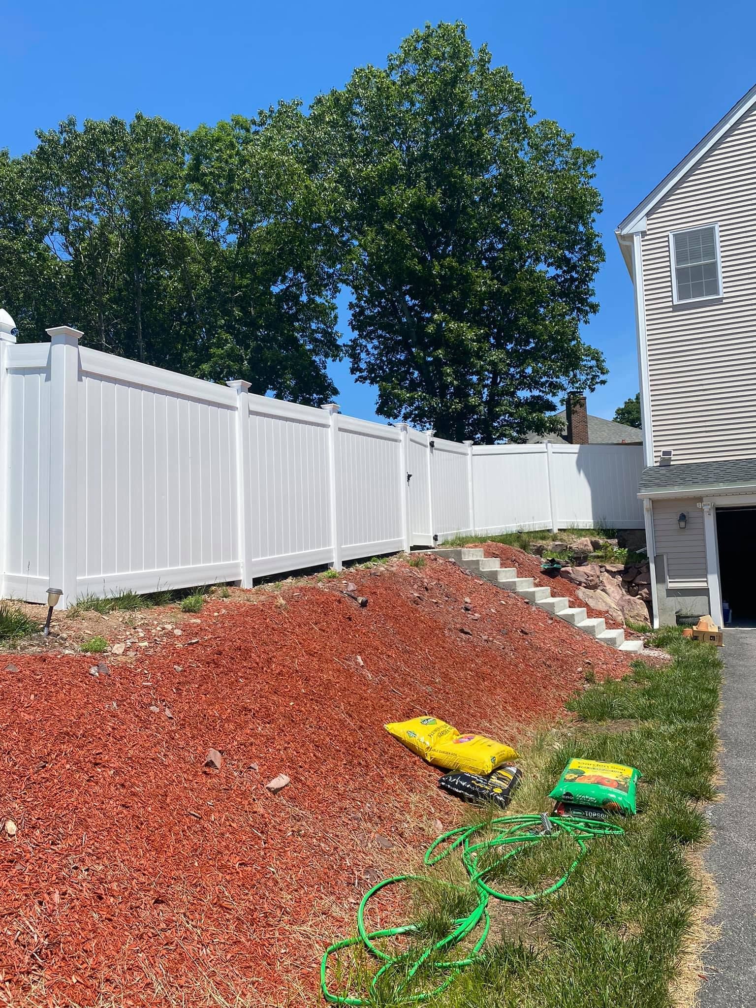 a white fence is surrounded by red mulch and a house .