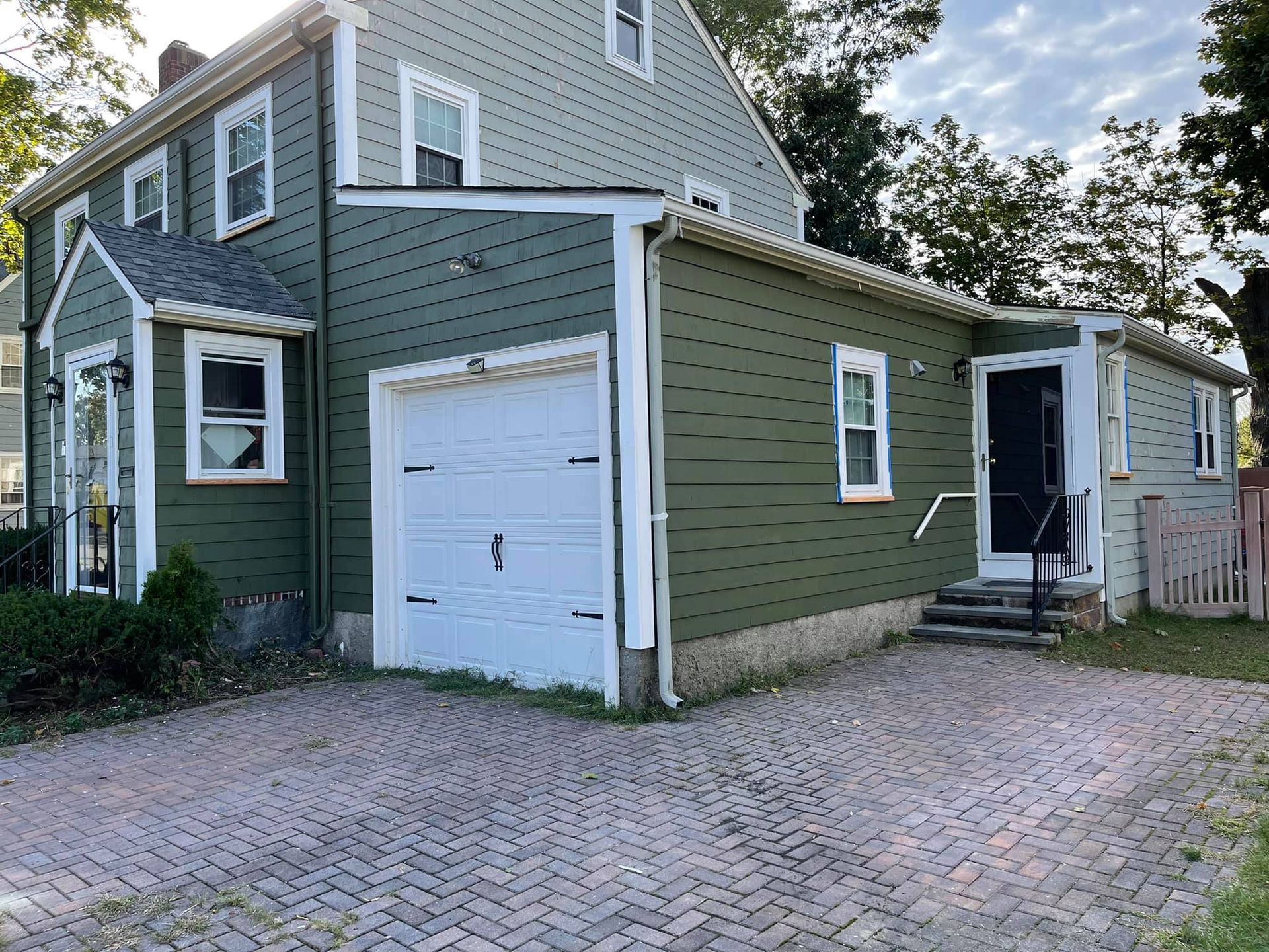 a green house with a white garage door and a brick driveway .