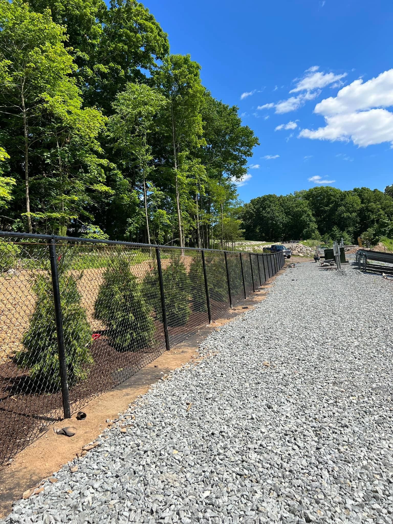 a chain link fence along a gravel road with trees in the background .