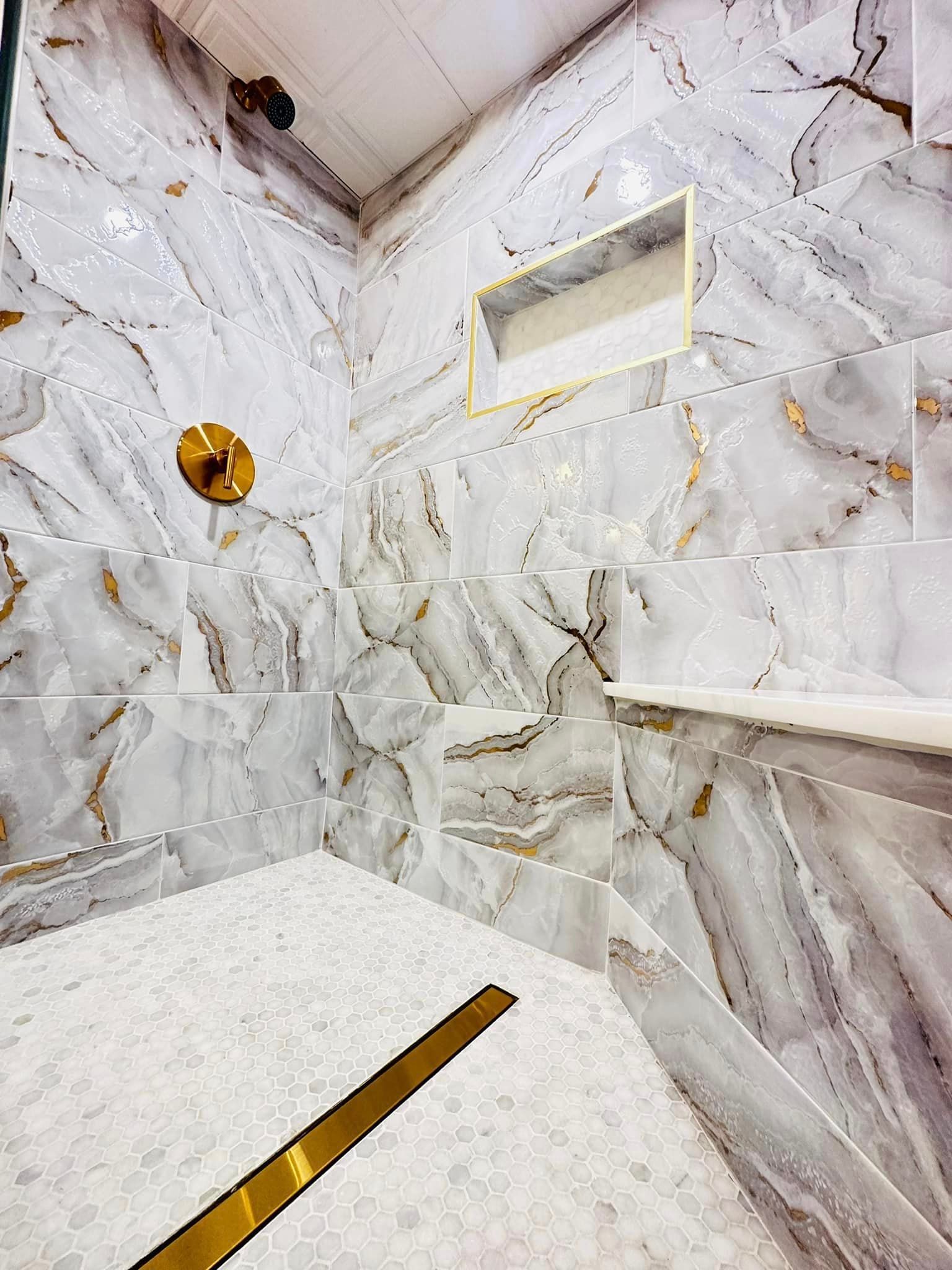 a bathroom with marble tiles and a walk in shower with a gold drain .