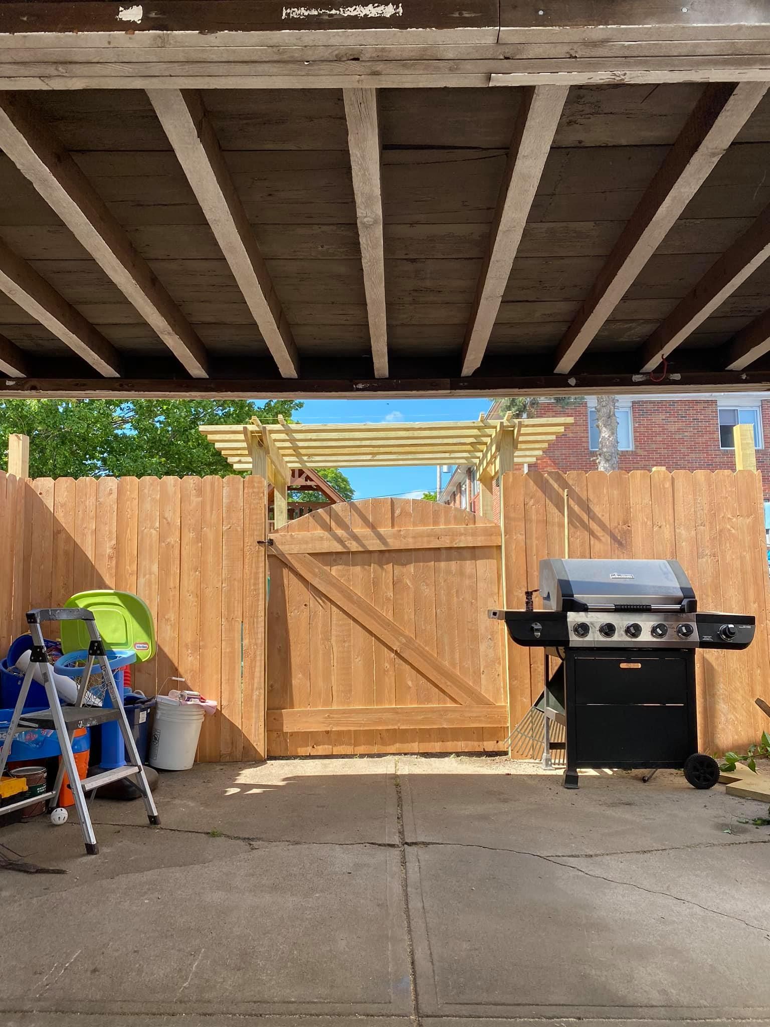a grill is sitting under a wooden fence in a backyard .