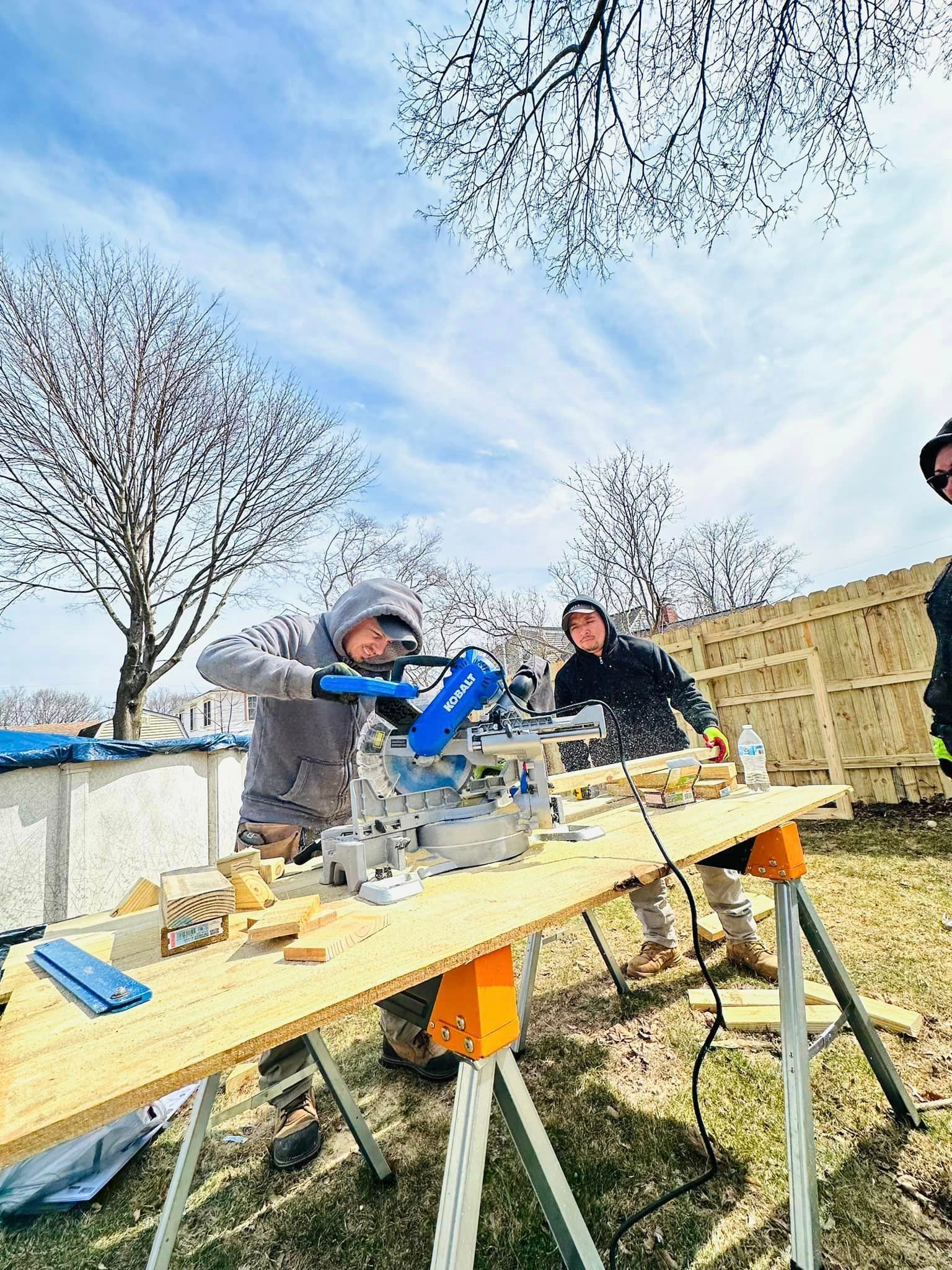 a group of people are working on a wooden table outside .