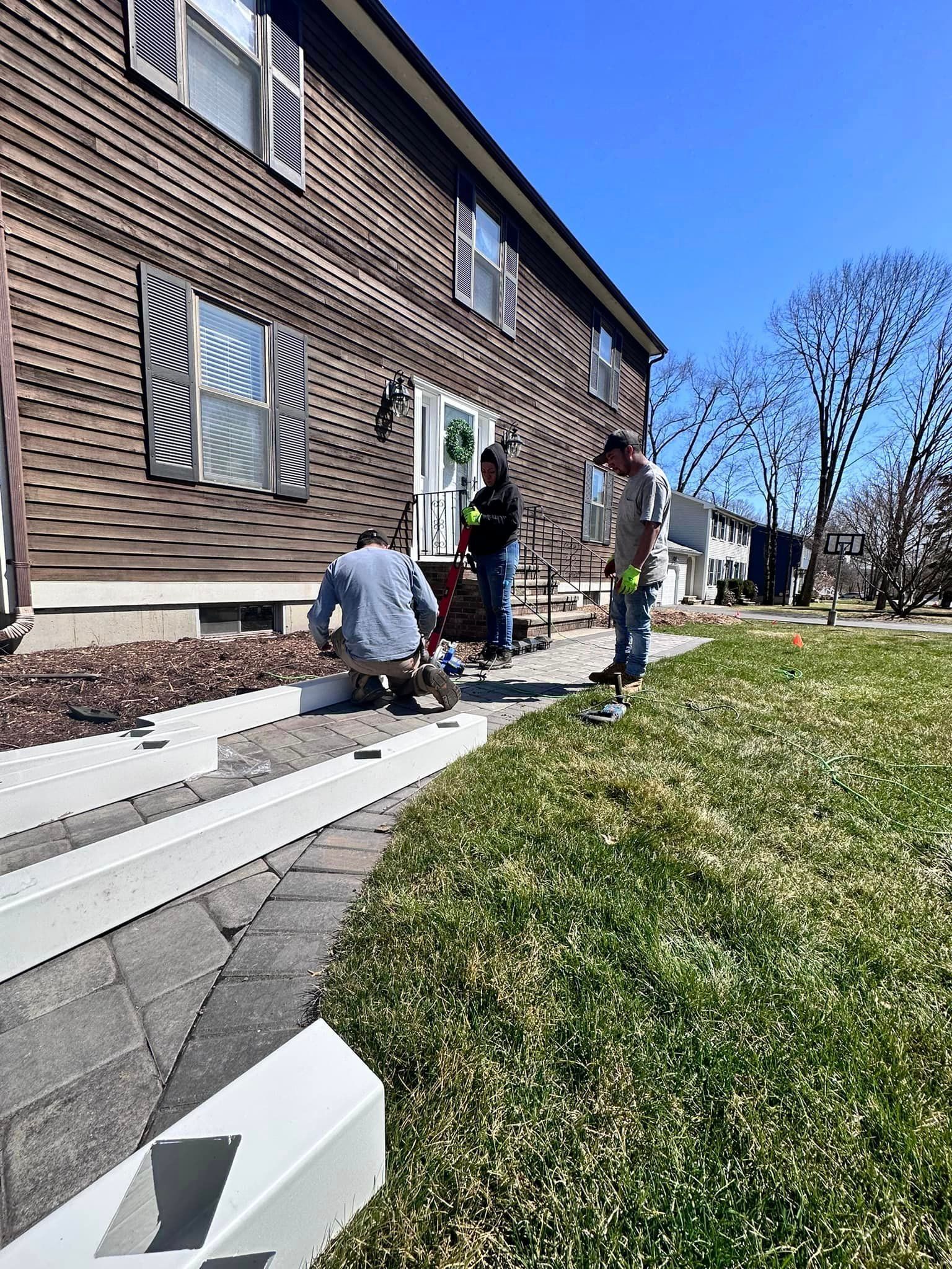 a group of people are working on a sidewalk in front of a house .